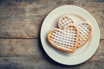 Two heart-shaped waffles dusted with powdered sugar on a plate
