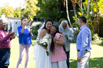 In garden, bride hugging woman as guests clapping and celebrating joyfully