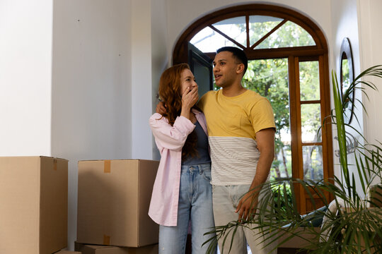 Young couple standing in new home surrounded by moving boxes, feeling excited