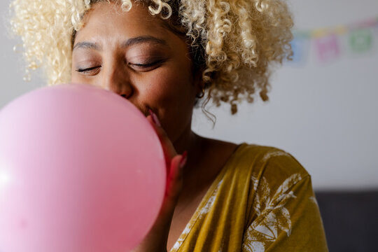 Woman blowing pink balloon at home, preparing for party celebration