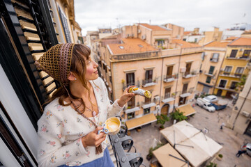 A young woman enjoys coffee and a Sicilian cannolo on a balcony overlooking narrow Palermo streets....