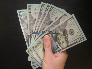A hand holding fan of US 100 dollar bills as a symbol of money, cash, dollar, pay, income and...
