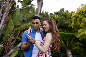 Young couple in garden admiring engagement ring, sharing joyful moment together