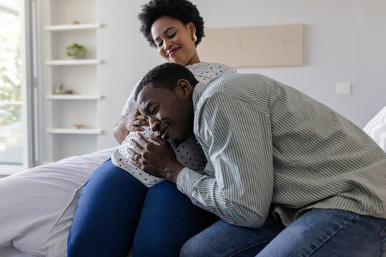 Expectant couple sharing tender moment at home, husband listening to wife's belly