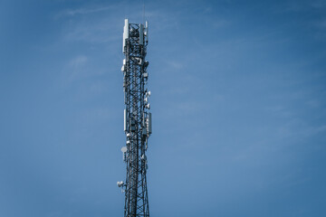 Obraz premium A tall communications tower equipped with antennas and satellite dishes stands sharply against a vivid blue sky, symbolizing modern technology and connectivity. Includes copy space.