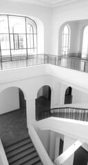 Interior view of a grand, multi-level hall with arched doorways, large windows, and a sweeping staircase.  Bright, airy space with clean lines
