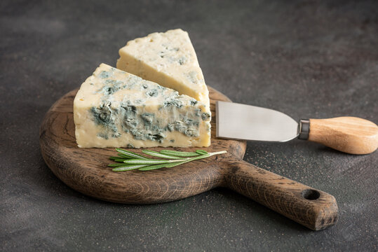 Pieces of blue cheese on wooden cutting board with rosemary and cheese knife, selective focus
