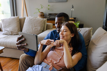 Couple relaxing at home, smiling and taking selfie with tablet on couch