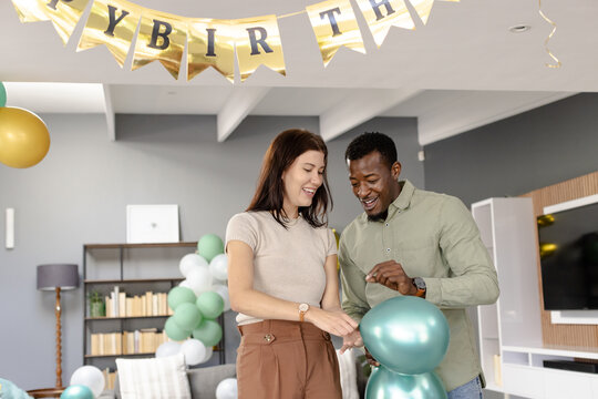 Couple decorating living room with balloons, preparing for birthday celebration