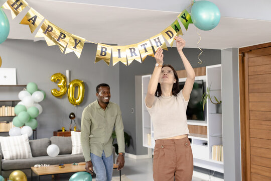 Decorating for birthday party, woman hanging banner while man smiling in living room