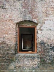 Aged brick wall architecture features a closed wooden window on an old building facade