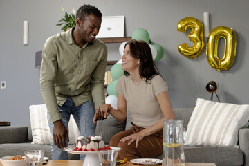 Celebrating birthday, African American man and woman smiling with cake and balloons