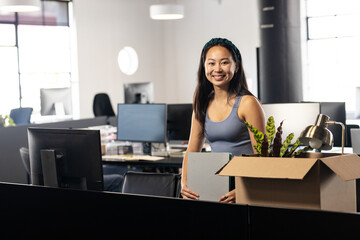 Woman unpacking plant  and  lamp from cardboard box at desk partition in open plan office
