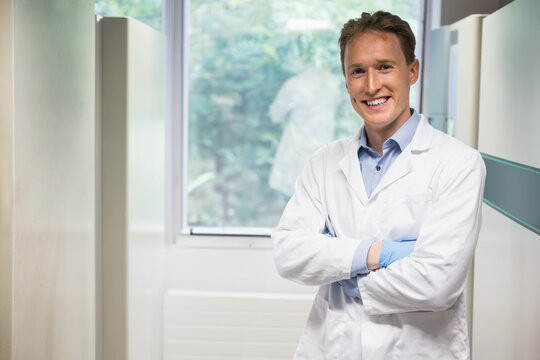 Smiling male doctor standing in lab corridor, with white lab coat and blue gloves, copy space