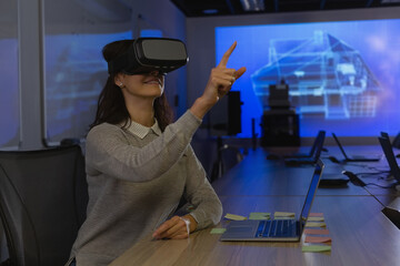 Engineer is wearing VR headset and pointing at car wireframe on screen above table in lab
