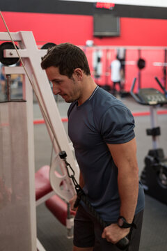 Athletic man performing tricep pushdown on cable pulley inside gym, with red and white wall stripes