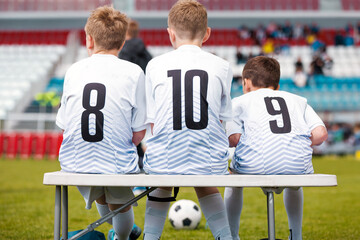 Young Soccer Players Wearing Jersey Numbers 8, 10, and 9 Sitting on Bench Before Match at Stadium