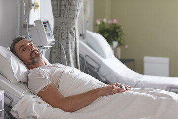 Resting senior man lying semi-upright in hospital room, with nasal cannula and IV stand, copy space