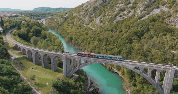 Aerial drone footage of a graffiti-covered train moving over the historic Sokanski Most (Solkan Bridge) in Slovenia. The world's largest stone arch railway bridge