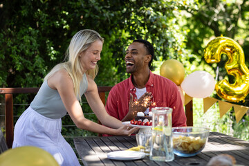 Celebrating birthday outdoors, friends sharing cake and laughter with festive decorations