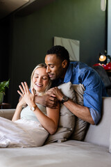 Couple celebrating engagement at home, smiling and embracing on cozy sofa