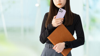スマートフォンとバインダーを持つ若い女性・ビジネスウーマン