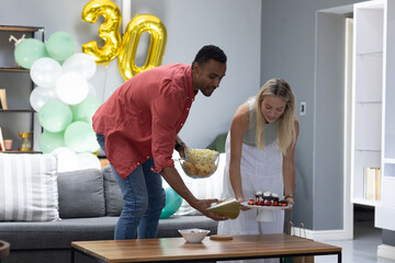 Obraz premium Celebrating birthday, couple arranging cake and snacks in living room with balloons
