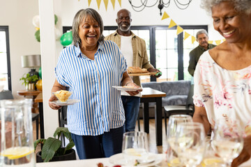 Smiling woman serving food at family gathering, celebrating in bright living room