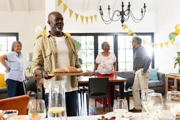 Elderly man serving bread at family gathering, smiling and enjoying celebration