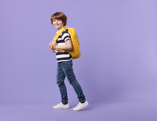 Cute schoolboy with backpack on violet background, space for text