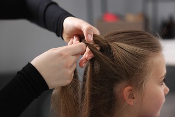 Fototapeta premium Hairstylist braiding girl's hair in salon, closeup