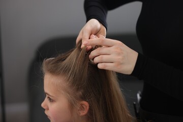 Naklejka premium Hairstylist braiding girl's hair in salon, closeup