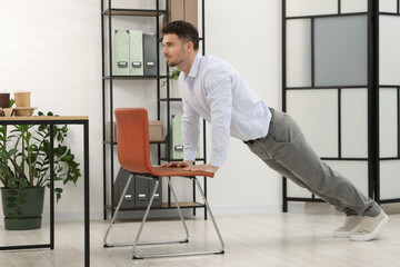 Handsome man exercising with chair in office