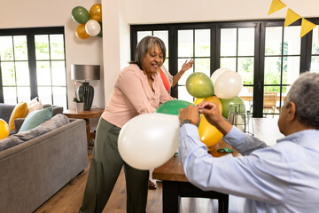 Senior couple decorating living room with colorful balloons for festive celebration