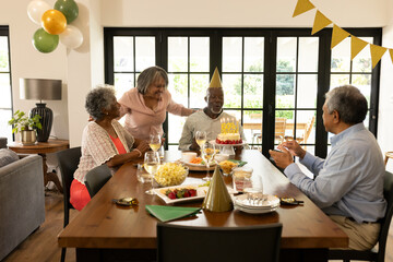 Celebrating birthday, elderly friends sharing cake and conversation at home together