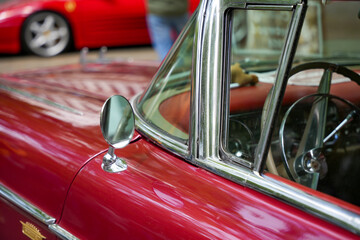 A chrome side mirror on a red convertible classic car. The mirror is mounted on the front fender,...