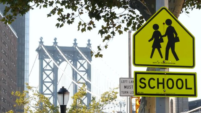 School zone yellow road sign, people crossing. Children safety on street, Manhattan downtown, New York City architecture. Education symbol USA. Pedestrians ahead, traffic roadsign and Manhattan Bridge