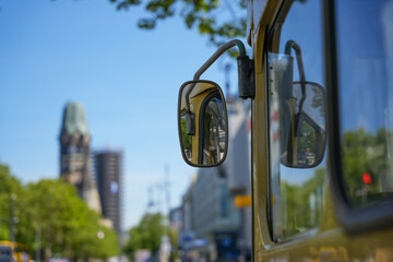 Mirror reflection on city street. Side mirror of a vintage bus reflecting the bustling urban...