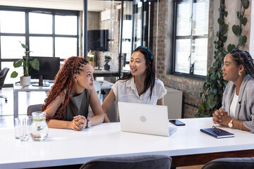 Diverse businesswomen discussing project at office table with laptop and notebooks