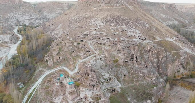 A drone approaches the rock-carved settlements in Kayseri Soğanlı Valley. Historical structures are intertwined with natural rock formations, approaching the window of the rock formation.