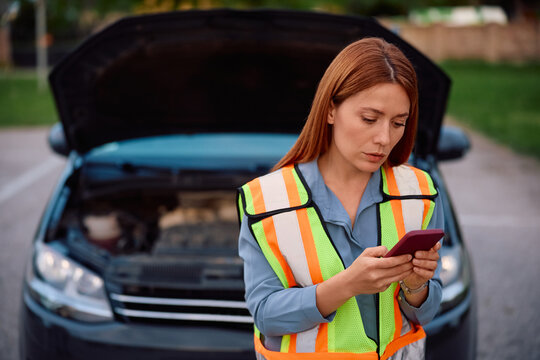 Female driver texting on cell phone after vehicle breakdown on road.