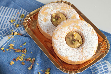 Shortbread dough biscuits with pistachio cream and nuts on gold paper plate. Dessert for party, celebration.
