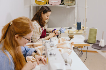 Two female seamstresses in the workshop at the factory are working at tables on sewing machines. fashion design, creating fashion collection for sale. shopping online. women are professional tailors.