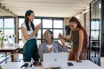 Colleagues celebrating success at office, smiling and clapping around laptop