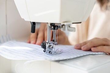 woman sews a light fabric on a sewing machine. making clothes, hobbies. a sewing studio, a clothing...