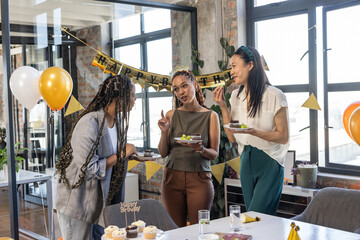 Colleagues enjoying birthday celebration with cake and decorations in modern office