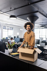 Smiling man unpacking box at modern office desk, starting new job