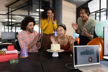 Celebrating birthday at office, diverse colleagues clapping around cake with candles