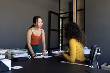 Two women discussing documents at office desk, collaborating on project