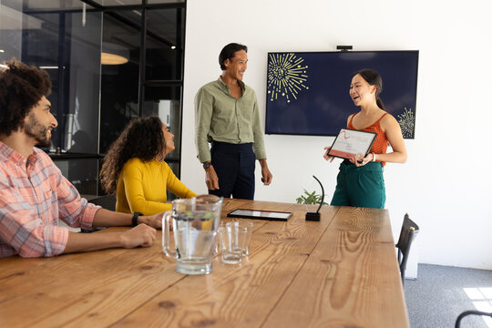 Receiving award, businesswoman smiling as colleagues applaud during office meeting